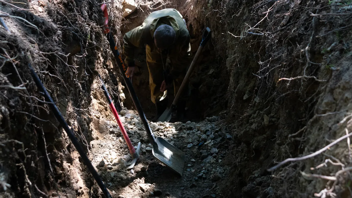 How to Route a Utility Trench Around Existing Underground Obstructions Worker in a deep trench with exposed roots on the sides